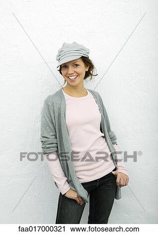 Stock Image - Young woman standing with thumbs in pockets, portrait. Fotosearch