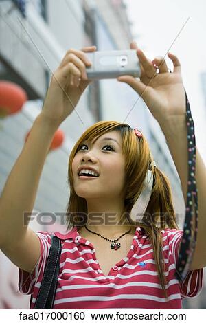 Stock Image - Young woman taking photo of self with cell phone. Fotosearch