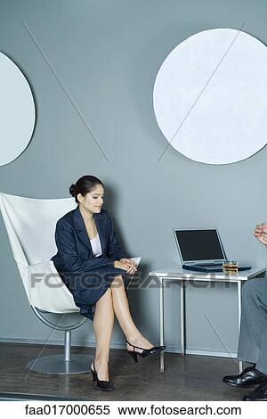 Stock Photography - Young woman wearing suit, sitting across from man with laptop and glass of whisky. Fotosearch