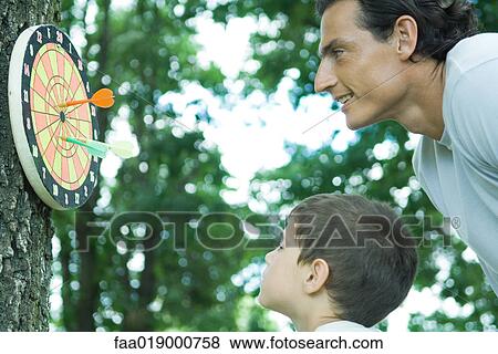 Boy and father looking at dartboard on tree View Large Photo Image Stock Photo - Boy and father looking at dartboard on tree. Fotosearch