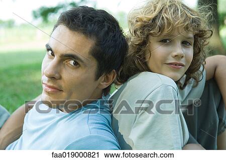 Stock Image - Boy and father sitting back to back. Fotosearch