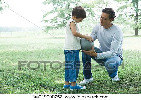 Stock Image - Boy and father talking outdoors, holding ball. Fotosearch