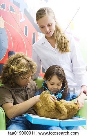 Stock Image - Boy and girl playing doctor with teddy bear. Fotosearch