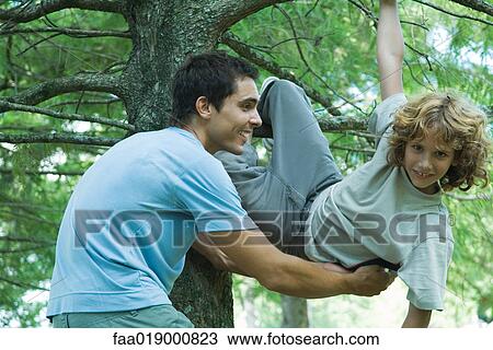 Boy climbing tree, father catching him View Large Photo Image Stock Image - Boy climbing tree, father catching him. Fotosearch