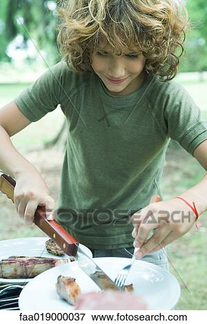 Stock Photo - Boy cutting up meat on plate. Fotosearch