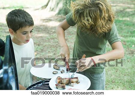 Boy cutting up meat on plate while second boy watches View Large Photo Image Stock Photo - Boy cutting up meat on plate while second boy watches. Fotosearch