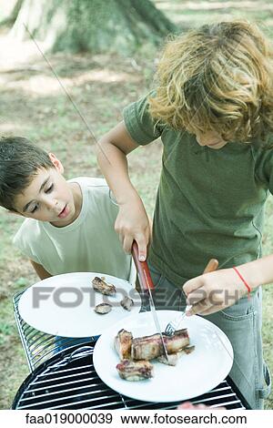 Stock Photo - Boy cutting up meat on plate while second boy watches. Fotosearch