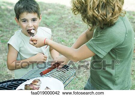 Boy feeding bite of grilled meat to younger boy View Large Photo Image Stock Image - Boy feeding bite of grilled meat to younger boy. Fotosearch