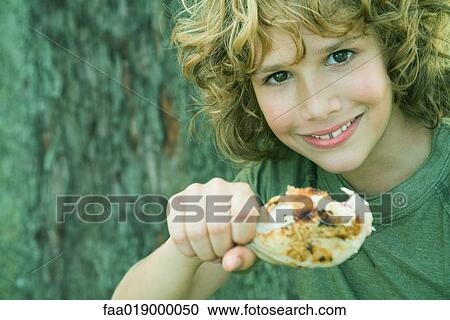 Stock Image - Boy holding grilled chicken leg, smiling at camera, portrait. Fotosearch