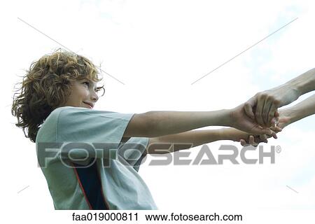 Stock Image - Boy holding hands with mother, partial view. Fotosearch