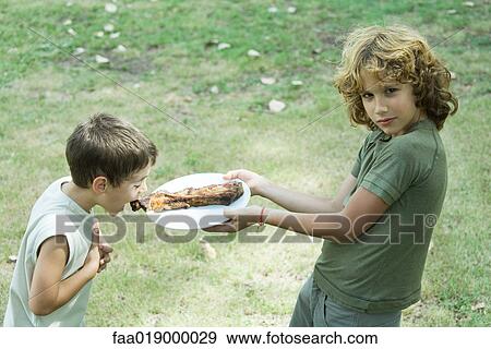 Boy holding up plate of grilled meat while second boy leans forward to take bite View Large Photo Image Stock Photo - Boy holding up plate of grilled meat while second boy leans forward to take bite. Fotosearch