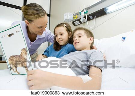 Stock Image - Boy in hospital bed, reading book with mother and sister. Fotosearch