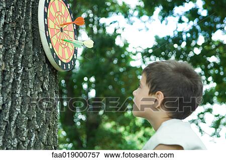 Boy looking at dart board on tree View Large Photo Image Stock Photo - Boy looking at dart board on tree. Fotosearch