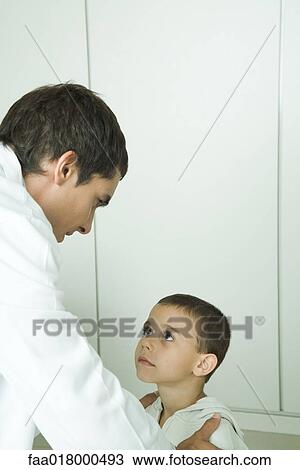 Stock Image - Boy looking up at doctor, doctor holding boy by shoulders. Fotosearch