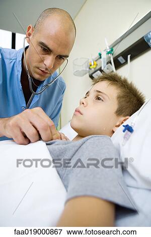 Boy lying in hospital bed, doctor listening to chest with stethoscope View Large Photo Image Stock Photo - Boy lying in hospital bed, doctor listening to chest with stethoscope. Fotosearch