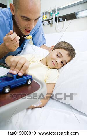 Stock Photo - Boy lying in hospital bed, doctor encouraging boy to eat meal. Fotosearch