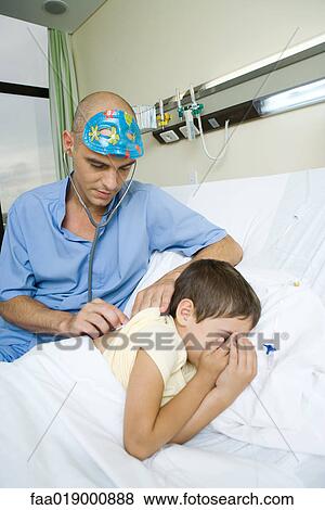 Boy lying in hospital bed, doctor listening to boy's back with stethoscope View Large Photo Image Stock Photo - Boy lying in hospital bed, doctor listening to boy's back with stethoscope. Fotosearch