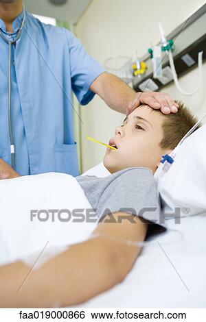 Stock Photograph - Boy lying in hospital bed, doctor taking temperature and feeling forehead. Fotosearch