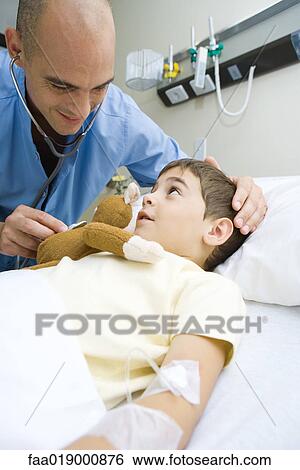 Stock Photograph - Boy lying in hospital bed, doctor holding stethoscope to stuffed monkey. Fotosearch