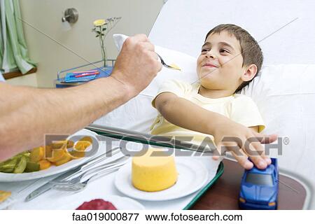 Stock Photo - Boy lying in hospital bed, eating meal. Fotosearch