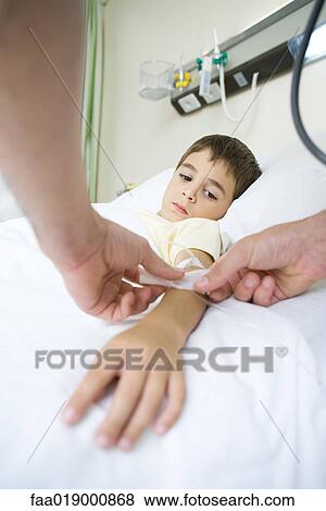 Stock Photo - Boy lying in hospital bed, having IV taped to arm. Fotosearch