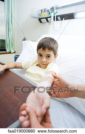 Stock Image - Boy lying in hospital bed, holding out arm. Fotosearch