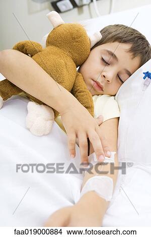 Boy lying in hospital bed, holding stuffed animal View Large Photo Image Picture - Boy lying in hospital bed, holding stuffed animal. Fotosearch