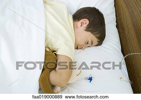 Boy lying in hospital bed, holding stuffed animal View Large Photo Image Stock Photo - Boy lying in hospital bed, holding stuffed animal. Fotosearch