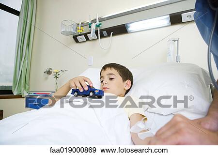 Boy lying in hospital bed, holding toy View Large Photo Image Stock Photo - Boy lying in hospital bed, holding toy. Fotosearch