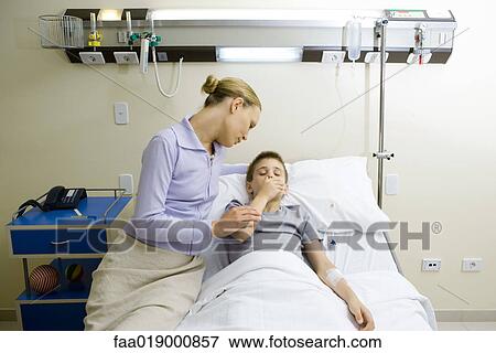 Stock Photo - Boy lying in hospital bed, mother sitting by side. Fotosearch