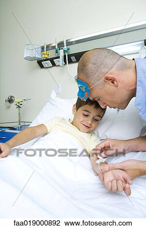 Stock Image - Boy lying in hospital bed, nurse adjusting IV. Fotosearch