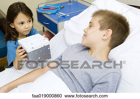Boy lying in hospital bed receiving present from girl View Large Photo Image Stock Image - Boy lying in hospital bed receiving present from girl. Fotosearch