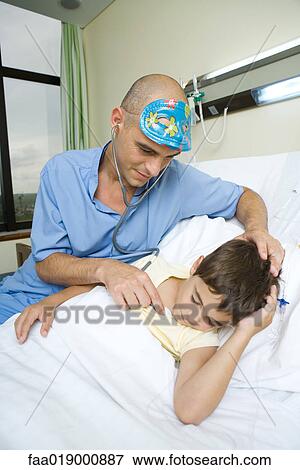 Boy lying in hospital bed, sleeping, doctor holding stethoscope to boy's chest View Large Photo Image Stock Photo - Boy lying in hospital bed, sleeping, doctor holding stethoscope to boy's chest. Fotosearch