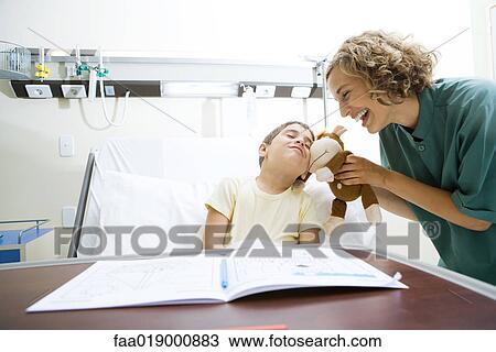 Boy lying in hospital bed, snuggling with stuffed animal nurse is holding up View Large Photo Image Stock Image - Boy lying in hospital bed, snuggling with stuffed animal nurse is holding up. Fotosearch