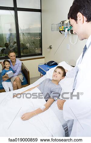 Boy lying in hospital bed surrounded by family and doctor View Large Photo Image Stock Photo - Boy lying in hospital bed surrounded by family and doctor. Fotosearch