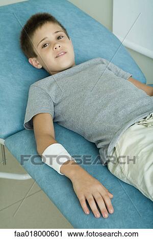 Stock Image - Boy lying on examination table with bandage around arm. Fotosearch