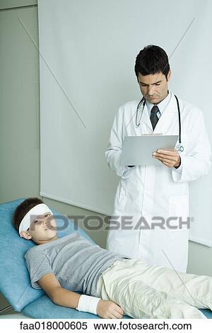 Boy lying on examination table with bandage on forehead and arm, doctor writing on clipboard View Large Photo Image Stock Photography - Boy lying on examination table with bandage on forehead and arm, doctor writing on clipboard. Fotosearch