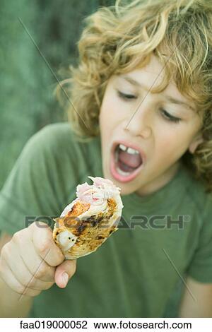 Stock Image - Boy ready to take a bite out of grilled chicken leg. Fotosearch