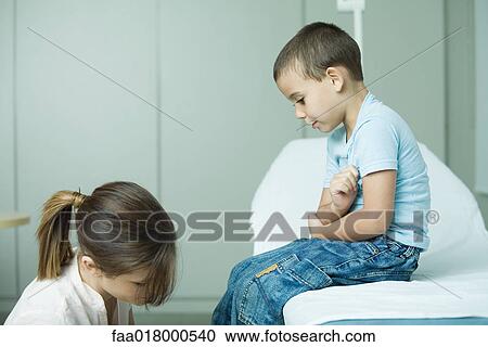 Stock Image - Boy sitting on examination table, looking down at nurse. Fotosearch