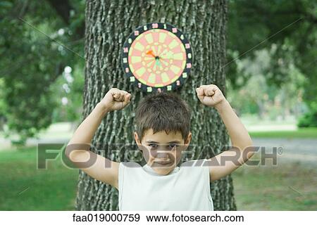 Boy standing in front of dart board on tree, arms up View Large Photo Image Stock Photo - Boy standing in front of dart board on tree, arms up. Fotosearch