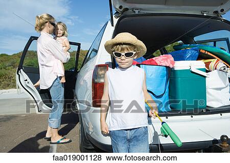 Stock Photo - Boy standing in front of loaded car trunk. Fotosearch