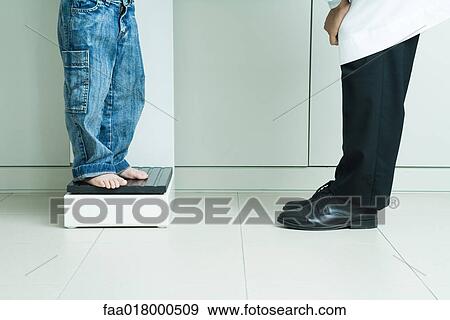 Stock Photo - Boy standing on scale, across from doctor, waist down. Fotosearch