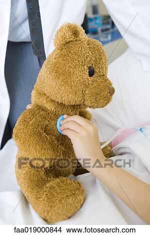 Child holding toy stethoscope to teddy bear, partial view View Large Photo Image Picture - Child holding toy stethoscope to teddy bear, partial view. Fotosearch