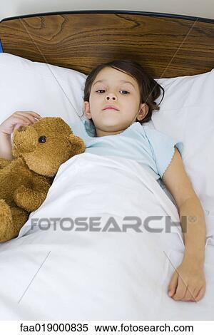 Stock Photography - Child lying in bed with teddy bear. Fotosearch