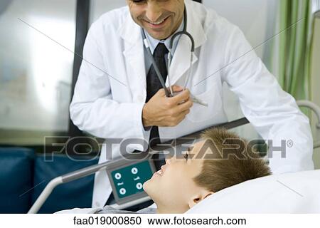 Stock Image - Child lying in hospital bed, doctor standing by side. Fotosearch