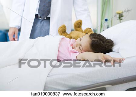 Stock Photo - Child lying in hospital bed, doctor standing by side. Fotosearch