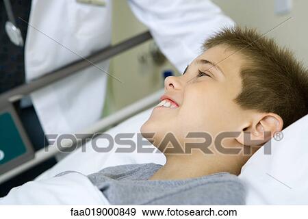 Stock Photo - Child lying in hospital bed, doctor standing by side. Fotosearch