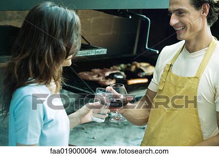 Picture - Couple clinking glasses next to barbecue. Fotosearch