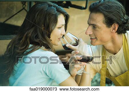 Stock Image - Couple drinking red wine with arms linked. Fotosearch