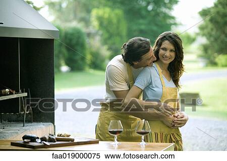 Stock Photography - Couple standing near outside wood oven, man holding woman from behind, putting head on her shoulder. Fotosearch